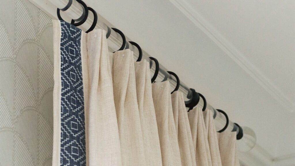 Close-up detail of custom leading edge banding on a linen drapery panel fabricated by Vitalia Inc., showing navy geometric trim and matte black ring hardware