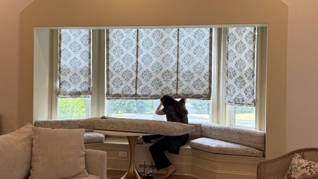 Custom motorized patterned Roman shades with coordinating upholstered bench and seat backs in a bay window nook, fabricated by Vitalia Inc. in collaboration with Ru & Co